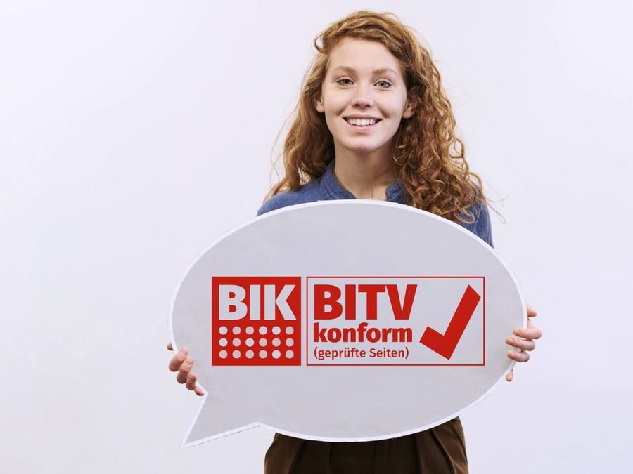 Großansicht Eine junge Frau hält eine Sprechblase hoch, auf der das Siegel BIK BITV-Konformität abgebildet ist