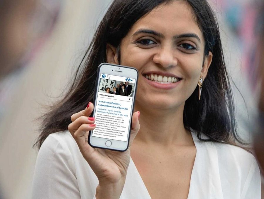 Eine Frau zeigt die barrierefreie Webseite der Stadt Meerbusch auf einem Smartphone