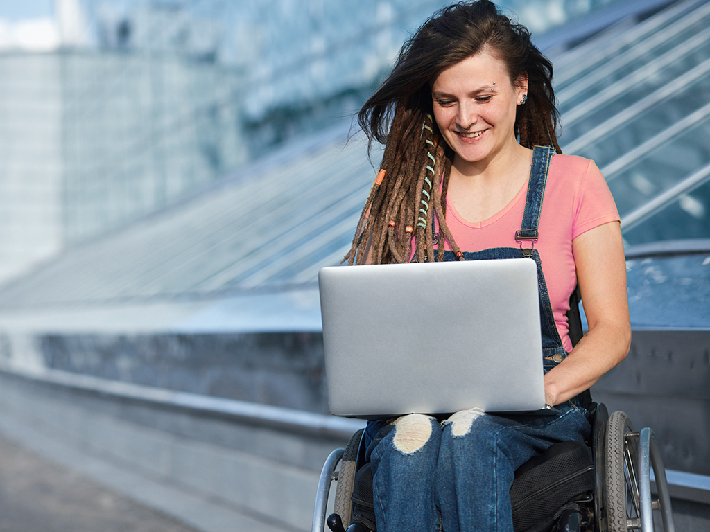 Junge Frau im Rollstuhl mit Laptop auf dem Schoß
